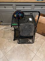 Front view showing glass top table, folded black Cosco step stool and disco light on floor in front of kitchen cabinetry.