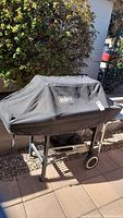 Weber gas grill covered with a black protective cover, situated outdoors on a patio.