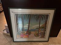 Frontal photo of framed beach-themed wall art showing palm trees, sea, and beach elements under glass within a dark green frame.