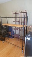 Full view of the wire rack showing the black metal frame, wood grain shelf, wheels, and side hooks