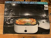 Front of the box showing the GE 18 Quart Roaster Oven with a cooked turkey and vegetables inside.