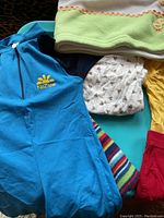 Photo of the blue NoZone sunscreen jumper, white pants with brown patterns, multi-colored striped knit hat, and parts of other clothing items piled together.
