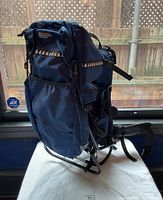 Photo showing right side of the blue baby carrier backpack with metal frame, padded straps, and side storage pocket.
