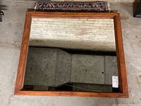 Rectangular antique mirror with wide pine frame. Shows reflections of brick wall and floor, frame has pine grain and natural finish with some wear.