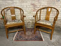 Full view of both chairs side by side on a small rug against a brick wall.