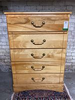 Front view of a solid blonde wood dresser with five drawers and brass handles.