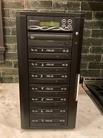 Front view of Spartan DVD duplicator with visible LCD screen, control buttons, and 7 DVD drives.