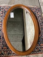 Top-down view of the full oval wood framed mirror placed on a patterned rug against a concrete floor.