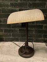 Side view of the bankers lamp showing textured glass shade, dark metal base, pull chain, and wrapped cord.