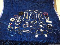 Lot of 44 assorted costume jewelry bracelets on blue fabric background showing overall assortment and variety of styles.