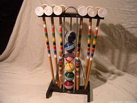 Full view of six wooden croquet mallets and six striped balls held on a plastic and metal rack