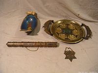 Overview photo showing all four Judaica items: brass Seder plate, brass fruit bowl, Star of David pendant, and scroll tube with chain, placed on neutral background.