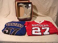 Photo showing folded NY Mets Santana jersey, folded Rutgers Ray Rice jersey, and box with houndstooth rain boots.