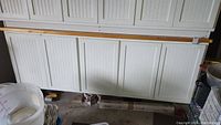 Wide view of closed white cabinet with pine top in garage, showing four panelled doors and some items on the left side.