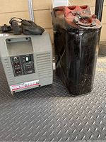 Gray Coleman Powermate Pulse 1850 portable generator next to a black and red metal jerry can on a patterned floor surface.