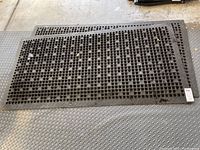 Three black rubber kitchen mats with grid holes placed on floor, showing full size and shape
