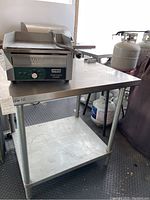 Full view of stainless steel commercial prep table with griddle on top and propane tanks in background, showing prep surface and structure.