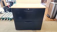 Front view of black metal two-drawer filing cabinet with beige top and lock on top drawer.