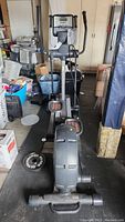 Front view of the NordicTrack elliptical in a garage setting surrounded by various items, showing console and handles.