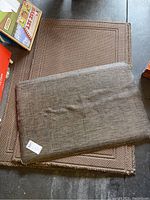Stack of brown rubber-backed mats including one smaller 2x3 ft mat on top of four larger 3x5 ft mats stacked below, showing condition and texture
