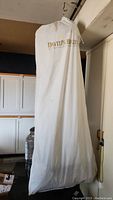David's Bridal branded garment bag protecting full length wedding dress hanging on a rack.