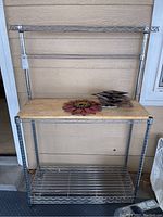 Full view of the stainless steel baker's rack with wooden cutting board top shelf and metal decorations on top.