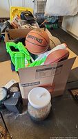 Box containing the basketball, football, green water blasters, and other toys in garage.