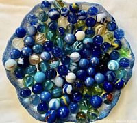 Top down image of 100 glass marbles in a decorative bowl showing various blue accent colors and patterns.