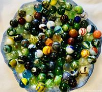 Top view of a circular arrangement of 100 assorted glass marbles showing their colors and patterns.