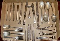Photo showing a set of silver plated specialty dining utensils including pearl handled knives, serving knives, spoons, forks, tongs, a condiment fork and decorative picks arranged in a box.