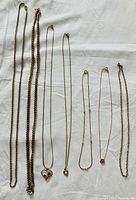 All 7 chain necklaces laid flat on white background showing varying lengths, thickness, and pendants.