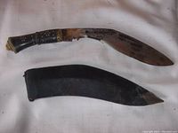 Front view of the curved steel kirpan blade and wood/bronze decorated grip alongside the black leather sheath with leather belt clip.