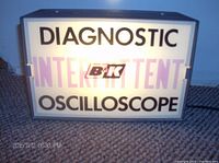 Photo of the front face of light box displaying the text 'DIAGNOSTIC INTERMITTENT B&K OSCILLOSCOPE' with light on, set on carpet.