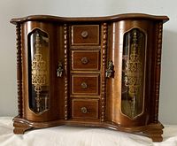 Front view of closed wooden jewelry box showing curved stencilled glass doors and central drawers.