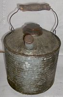 Front and side angle showing metal spout, screw cap lid, wire handle with wooden grip, and the hammered metal texture.