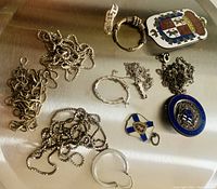 Image showing various sterling silver jewelry pieces including chains, rings, and enamel pendants placed on a reflective surface.