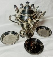 Photo showing vintage Forbes Silver Co. spooner with sugar bowl and lid, 10 silver spoons, and 3 silver plated coasters arranged around set on white background