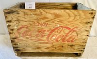 Front view of the wooden Coca-Cola crate showing faded red logo and wood grain.