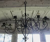 Side view of the chandelier hanging showing the 8 candle holders and wrought iron scrolling design.