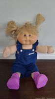Front view of Cabbage Patch doll with blonde pigtails, blue overalls, and pink shoes.