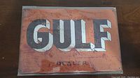 Photo of the rectangular metal Gulf dealer sign with large GULF lettering and smaller DEALER wording on orange background.