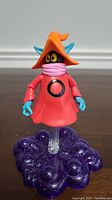 Front view of Orko action figure in red robe and orange hat on purple cloud stand