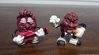 Front view of two California Raisins figures, one with red guitar and sunglasses, the other holding microphone.