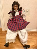 Front view of old-fashioned Christmas doll seated, showing outfit details and facial features.