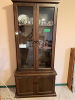 Front view of the tall narrow wooden cabinet showing glass doors with shelves inside and lower wooden doors.