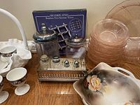 Overview of assorted glassware, ceramic dishes, and metal trivets on wooden table