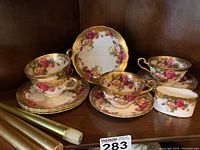 Overall view of four cups, four saucers and sugar bowl on wooden shelf