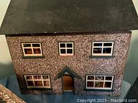 Exterior front view of the miniature stucco dollhouse showing speckled walls, green window and door trim, and black roof.