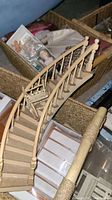 Close up of a curved wooden staircase miniature with carved banisters and a small miniature chair on the stairs.