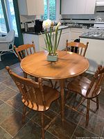 Photo of round wooden kitchen table with four matching wooden spindle-back chairs in kitchen setting.
